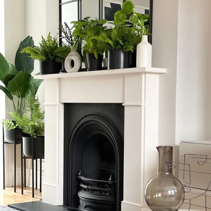 Ferns covering the top of a fire place and a large fern and birds of paradise plant in plant stands next to the fireplace.